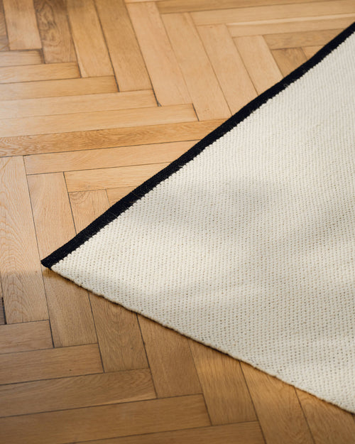 noo.ma handgeweven vloerkleed van Nieuw-Zeelandse wol, beige met Vulcano Black randaccent - rechthoekig, laagpolig 1 cm