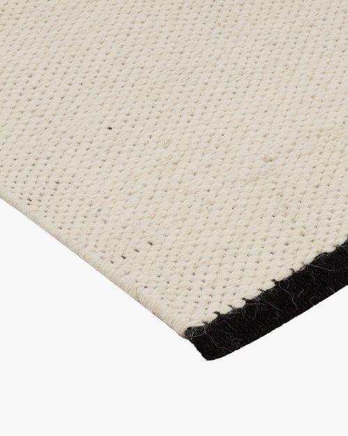 noo.ma handgeweven vloerkleed van Nieuw-Zeelandse wol, beige met Vulcano Black randaccent - rechthoekig, laagpolig 1 cm