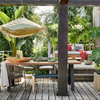 Stijlvol balkon met moderne buitentafel, rotan stoelen en decoratief dienblad met ananas, grenzend aan een verhoogde loungeplek met lichtgrijze kussens en botanische accenten.