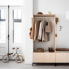 Scandinavisch ingerichte hal met naturel houten garderobekast, zachtbruine en beige kledingstukken, witgelakte dubbele deur en retro loopfietsje op een lichte gietvloer.