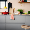 Moderne keuken met matgrijze greeploze keukenkasten, wit werkblad en gouden kraan, gestyled met rode gietijzeren pan, verse kruiden en houten snijplanken.